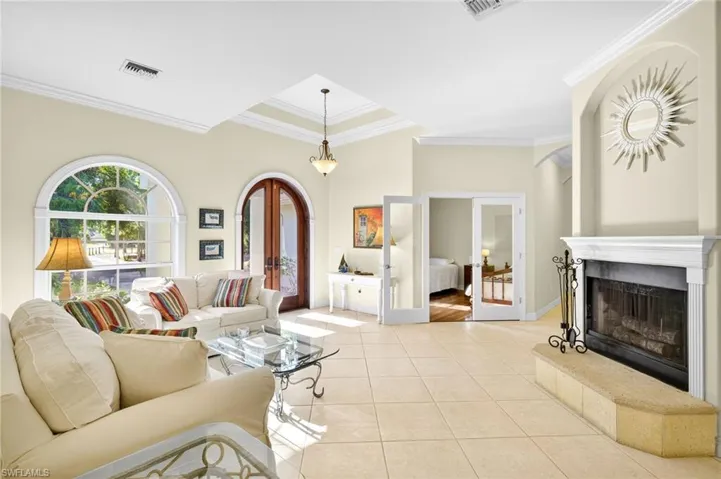 Living area featuring french doors, crown molding, light tile patterned flooring, and a fireplace