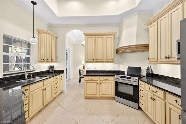 Kitchen featuring ornamental molding, electric stove, hanging light fixtures, light tile patterned floors, and wall chimney exhaust hood