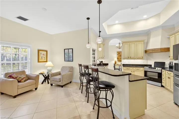Kitchen with cream cabinets, dark countertops, open floor plan, light tile patterned flooring, and a kitchen breakfast bar