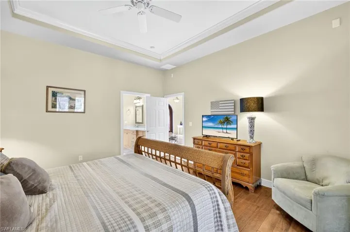 Bedroom with ornamental molding, wood finished floors, a tray ceiling, ensuite bath, and ceiling fan