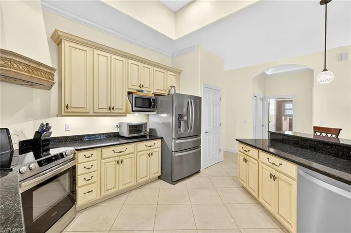 Kitchen with cream cabinetry, premium range hood, appliances with stainless steel finishes, arched walkways, and light tile patterned floors