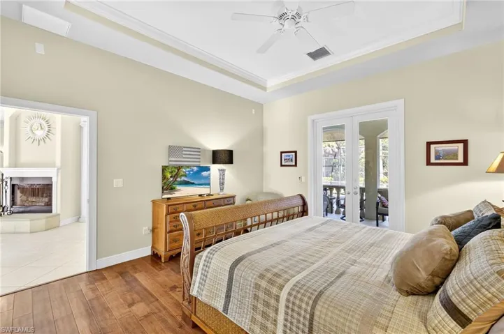 Bedroom with crown molding, wood finished floors, a raised ceiling, access to outside, and a fireplace