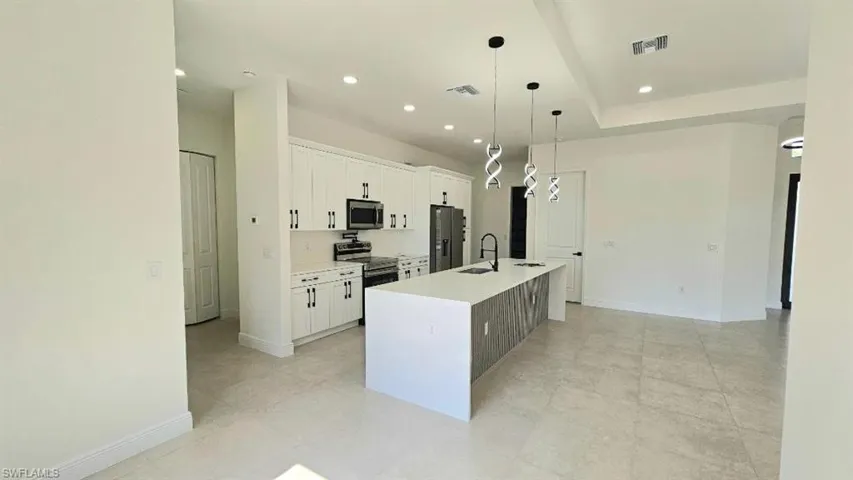 Kitchen featuring stainless steel appliances, a sink, a kitchen island with sink, white cabinets, and light countertops