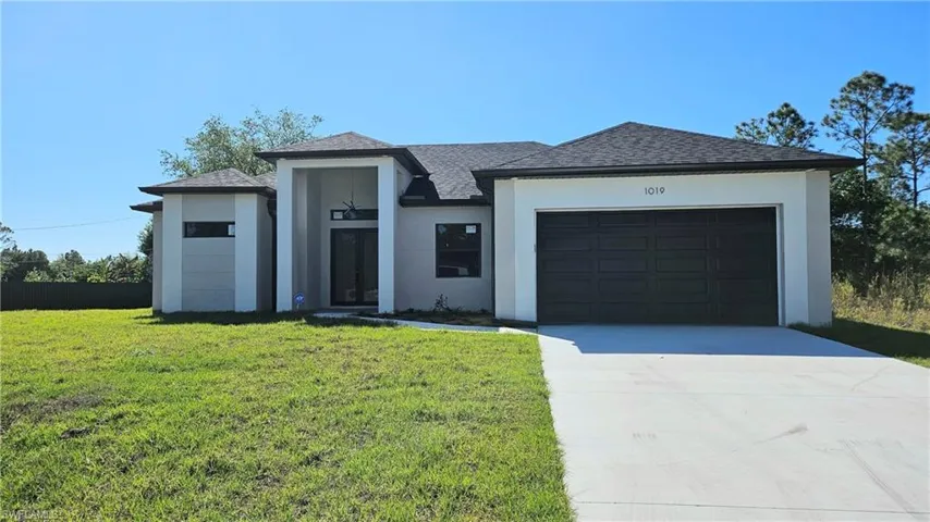 View of front of home with stucco siding, concrete driveway, a garage, a shingled roof, and a front yard