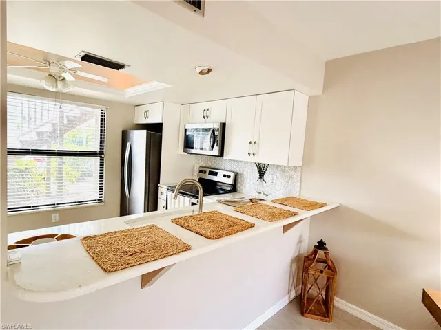 Kitchen with white cabinetry, stainless steel appliances, tasteful backsplash, ceiling fan, and a kitchen breakfast bar