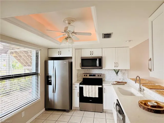 Kitchen with stainless steel appliances, white cabinets, light tile patterned floors, a ceiling fan, and a tray ceiling