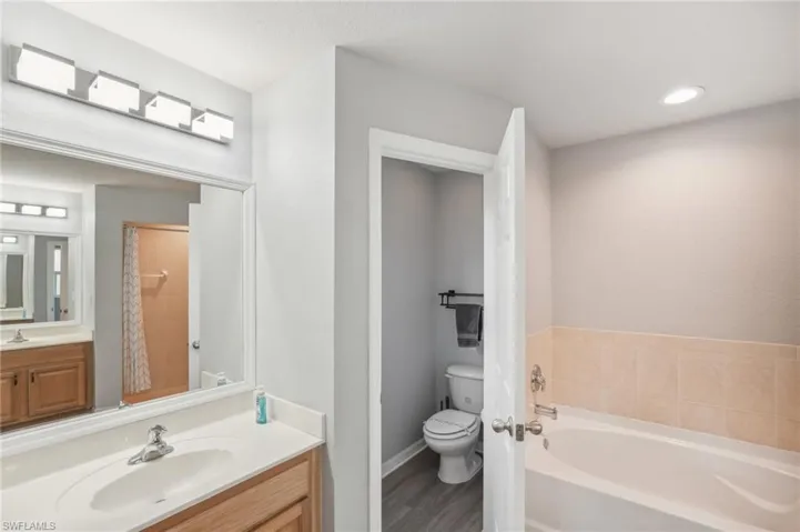 Full bath featuring a garden tub, vanity, a shower with shower curtain, and wood finished floors
