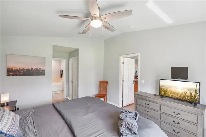 Bedroom with vaulted ceiling, a ceiling fan, ensuite bath, and light wood-style floors