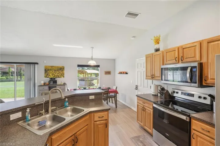 Kitchen featuring stainless steel appliances, dark countertops, lofted ceiling, decorative light fixtures, and light wood-style floors