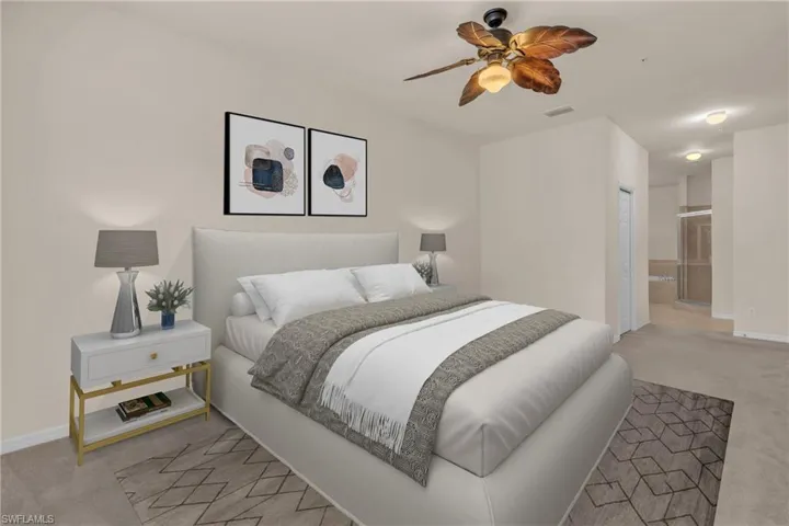 ViBedroom featuring light colored carpet, ensuite bath, and a ceiling fan