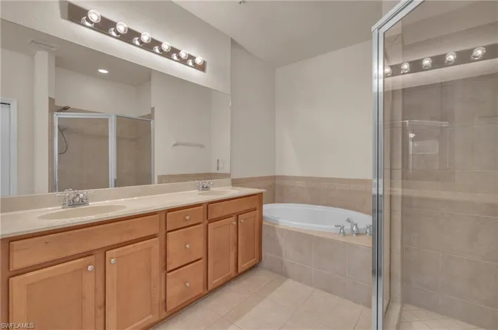 Full bathroom featuring a bath, double vanity, light tile patterned floors, and a stall shower