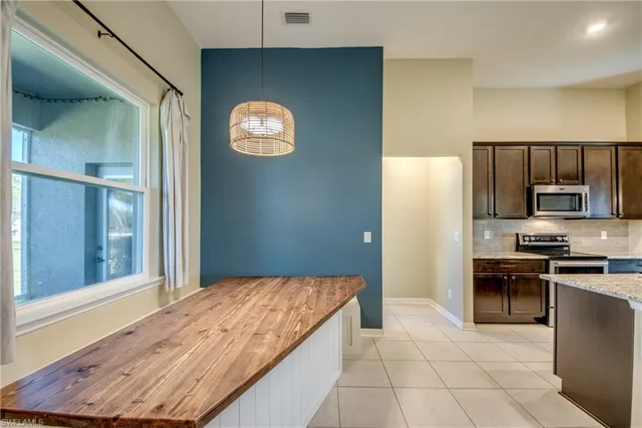 Kitchen featuring stainless steel appliances, dark wood finish cabinetry, light tile patterned flooring, light stone countertops, and decorative backsplash