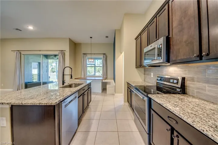 Kitchen with stainless steel appliances, dark wood finish cabinets, light stone counters, and a center island with sink