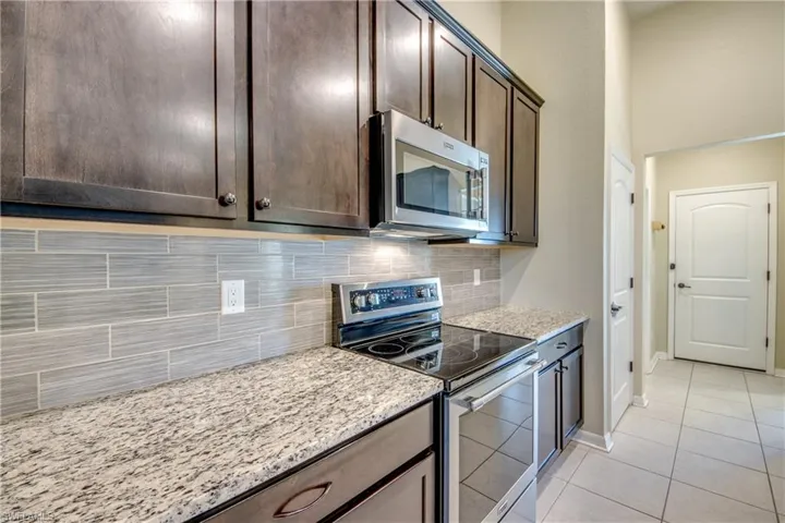 Kitchen with stainless steel appliances, dark wood finish cabinetry, light stone counters, light tile patterned flooring, and backsplash