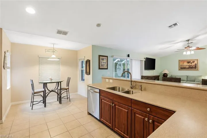 Virtually Staged Open-concept kitchen and dining area featuring a breakfast bar with a double basin sink, dark wood-finish cabinetry, and stainless steel dishwasher