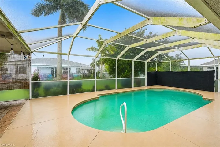 Virtually Staged Screened outdoor pool area featuring a freeform pool, integrated pool steps, and a surrounding concrete patio