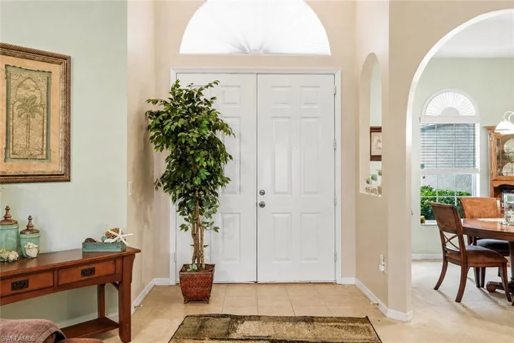 Virtually Staged Entryway featuring double white paneled doors with an arched transom window above, tile flooring, and arched interior doorways