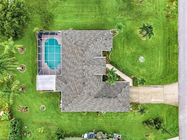 Expansive property featuring a screened-in swimming pool, shingle roof, mature landscaping, and a concrete driveway
