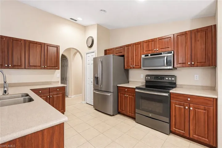Virtually Staged Kitchen featuring wood-finish cabinetry, stainless steel appliances, light-toned countertops, a double basin sink with a gooseneck faucet, and tile flooring