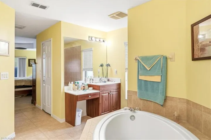 Bathroom featuring a built-in corner soaking tub, a dual-sink vanity with a dedicated seated area, a large wall-mounted mirror, and tile flooring