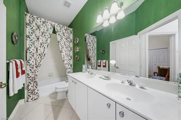 Bathroom featuring shower / tub combo with curtain, double vanity, and light tile patterned floors