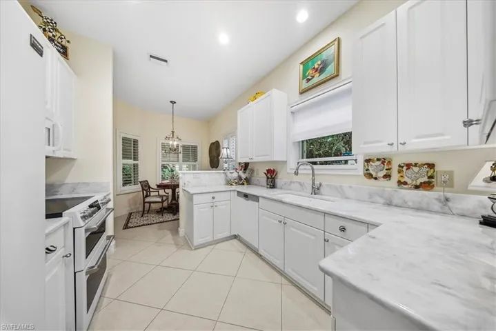 Kitchen with white appliances, white cabinets, pendant lighting, light tile patterned floors, and healthy amount of natural light