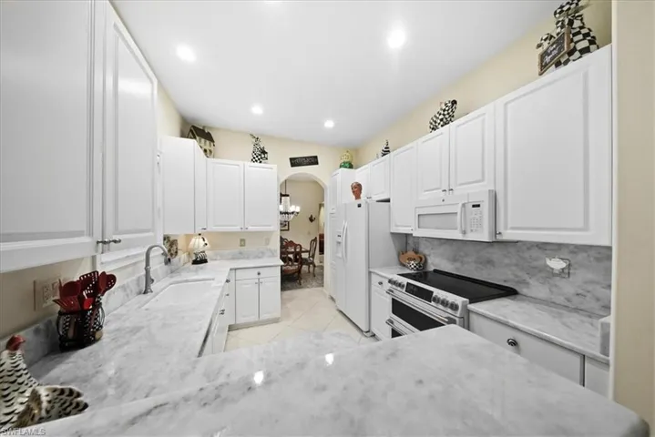 Kitchen featuring white cabinets, arched walkways, range with two ovens, white microwave, and recessed lighting