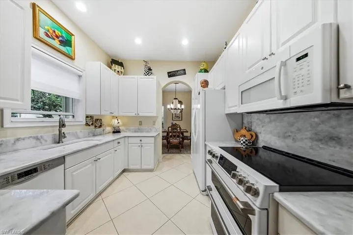 Kitchen featuring white appliances, arched walkways, a chandelier, white cabinets, and light tile patterned floors