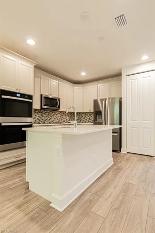 Kitchen featuring backsplash, a center island with sink, light hardwood / wood-style flooring, appliances with stainless steel finishes, and white cabinetry