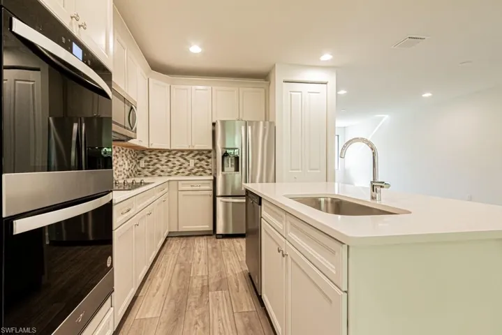Kitchen featuring appliances with stainless steel finishes, a kitchen island with sink, sink, white cabinets, and light hardwood / wood-style floors