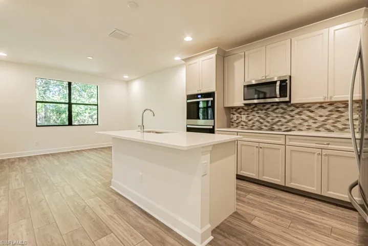 Kitchen featuring a kitchen island with sink, sink, appliances with stainless steel finishes, light hardwood / wood-style floors, and white cabinetry