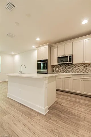 Kitchen with white cabinetry, a center island with sink, light wood-type flooring, and appliances with stainless steel finishes