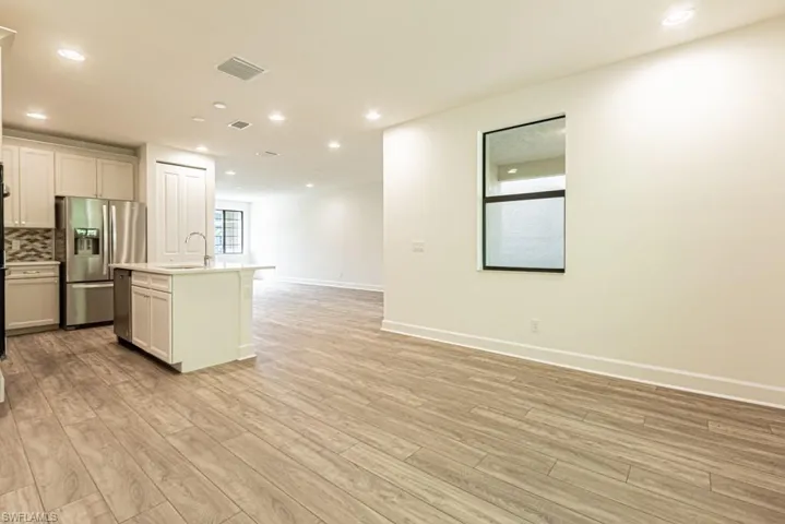Kitchen with light hardwood / wood-style floors, tasteful backsplash, stainless steel appliances, and an island with sink