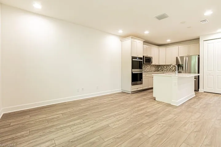 Kitchen with white cabinetry, light hardwood / wood-style flooring, stainless steel appliances, and a center island with sink