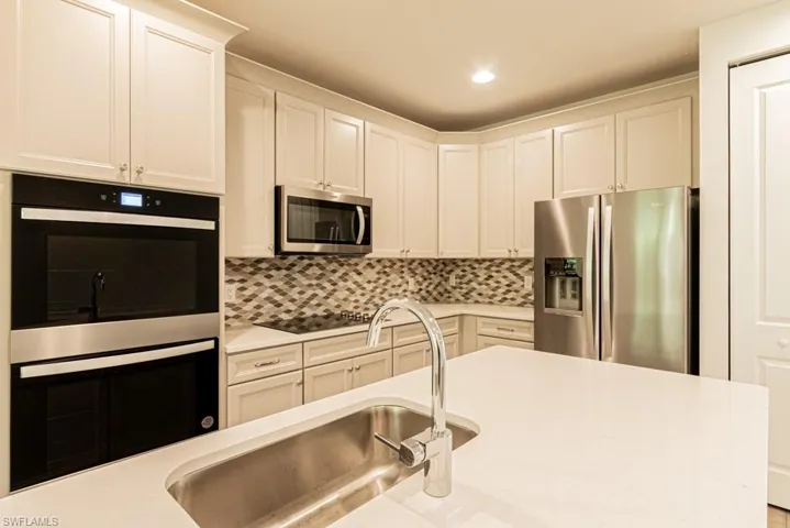 Kitchen featuring backsplash, sink, white cabinets, and appliances with stainless steel finishes