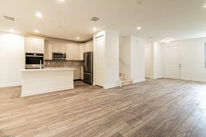 Kitchen featuring decorative backsplash, appliances with stainless steel finishes, a center island with sink, light hardwood / wood-style floors, and white cabinetry