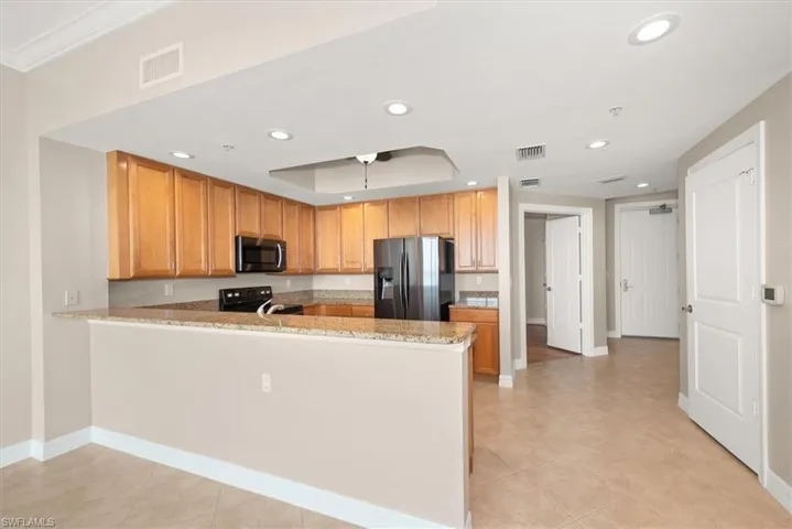Kitchen with a peninsula, stainless steel refrigerator with ice dispenser, light stone counters, light tile patterned floors, and recessed lighting