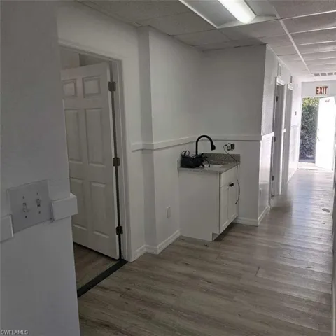 Corridor featuring wood finished floors, a drop ceiling, a sink, and baseboards