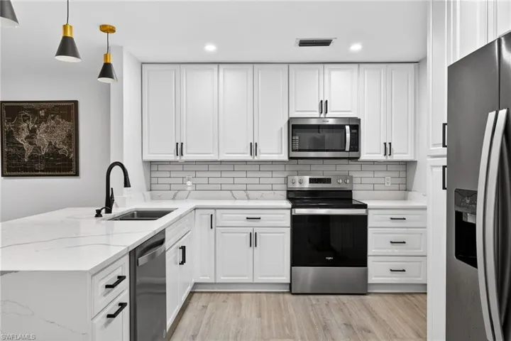 Kitchen with stainless steel appliances, backsplash, white cabinetry, a peninsula, and light stone countertops