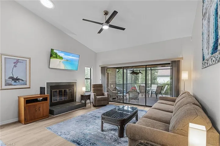 Living room with ceiling fan, light hardwood / wood-style floors, high vaulted ceiling, and a tiled fireplace