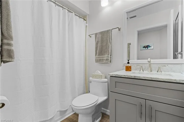 Full bathroom with toilet, vanity, shower / tub combo with curtain, and hardwood / wood-style flooring