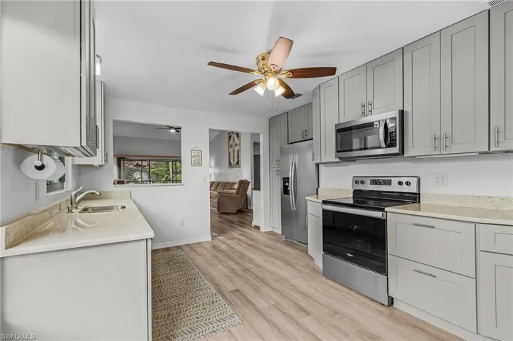 Kitchen with gray cabinetry, ceiling fan, sink, stainless steel appliances, and light hardwood / wood-style flooring