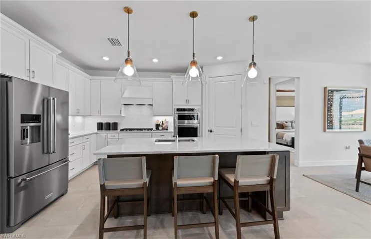 Kitchen with stainless steel appliances, a breakfast bar, light stone counters, an island with sink, and tasteful backsplash