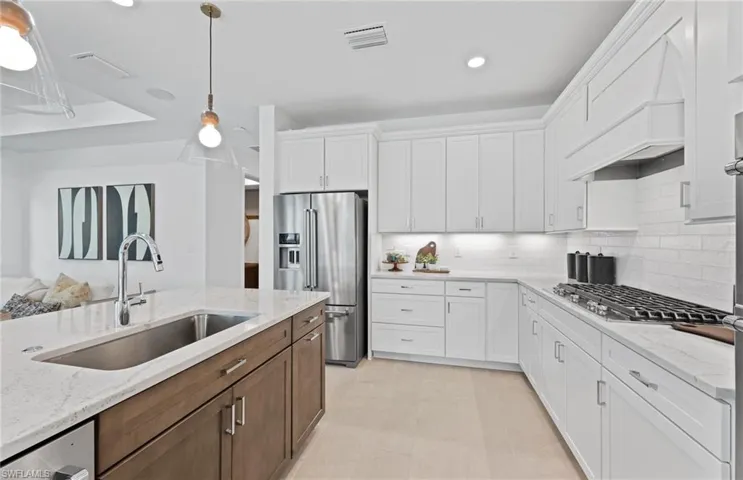 Dual tone kitchen with two tone color scheme, light stone counters, hanging light fixtures, stainless steel appliances, and decorative backsplash