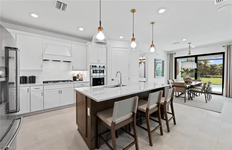 Kitchen featuring two tone cabinets, a breakfast bar, light stone counters, stainless steel appliances, and a kitchen island with sink