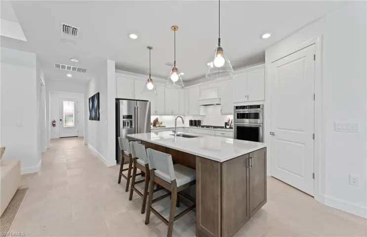 Kitchen featuring a center island with sink, light stone counters, a breakfast bar area, stainless steel appliances, and hanging light fixtures