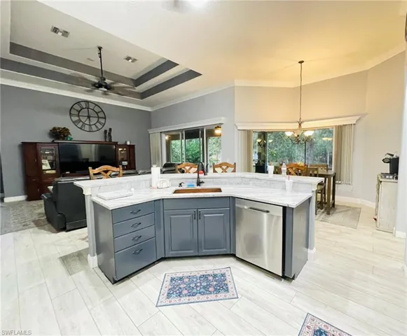 Kitchen featuring a kitchen island with sink, dishwasher, crown molding, light stone countertops, and open floor plan