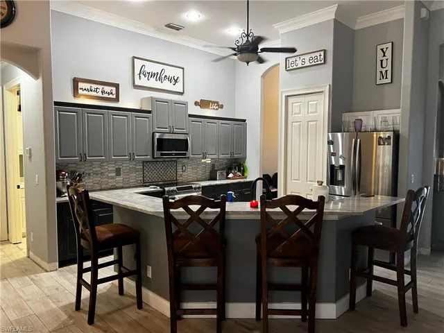Kitchen featuring arched walkways, ornamental molding, light wood finished floors, gray cabinetry, and recessed lighting