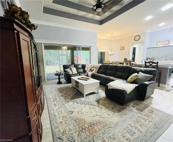 Living area featuring a raised ceiling, ceiling fan, ornamental molding, a chandelier, and arched walkways