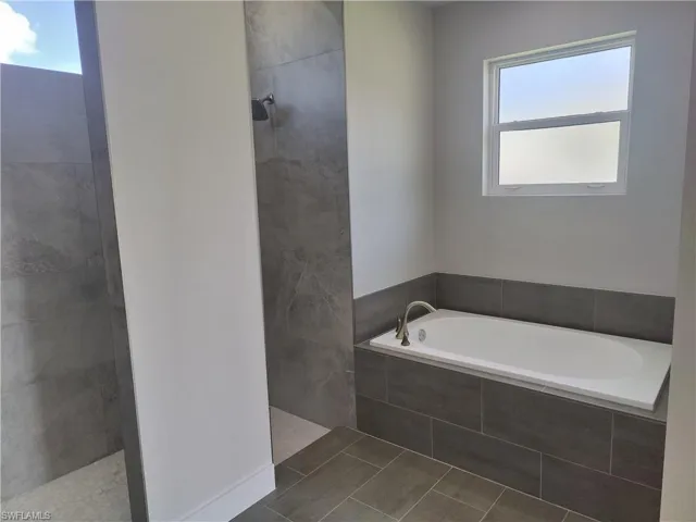 Bathroom featuring walk in shower, a garden tub, healthy amount of natural light, and tile patterned flooring